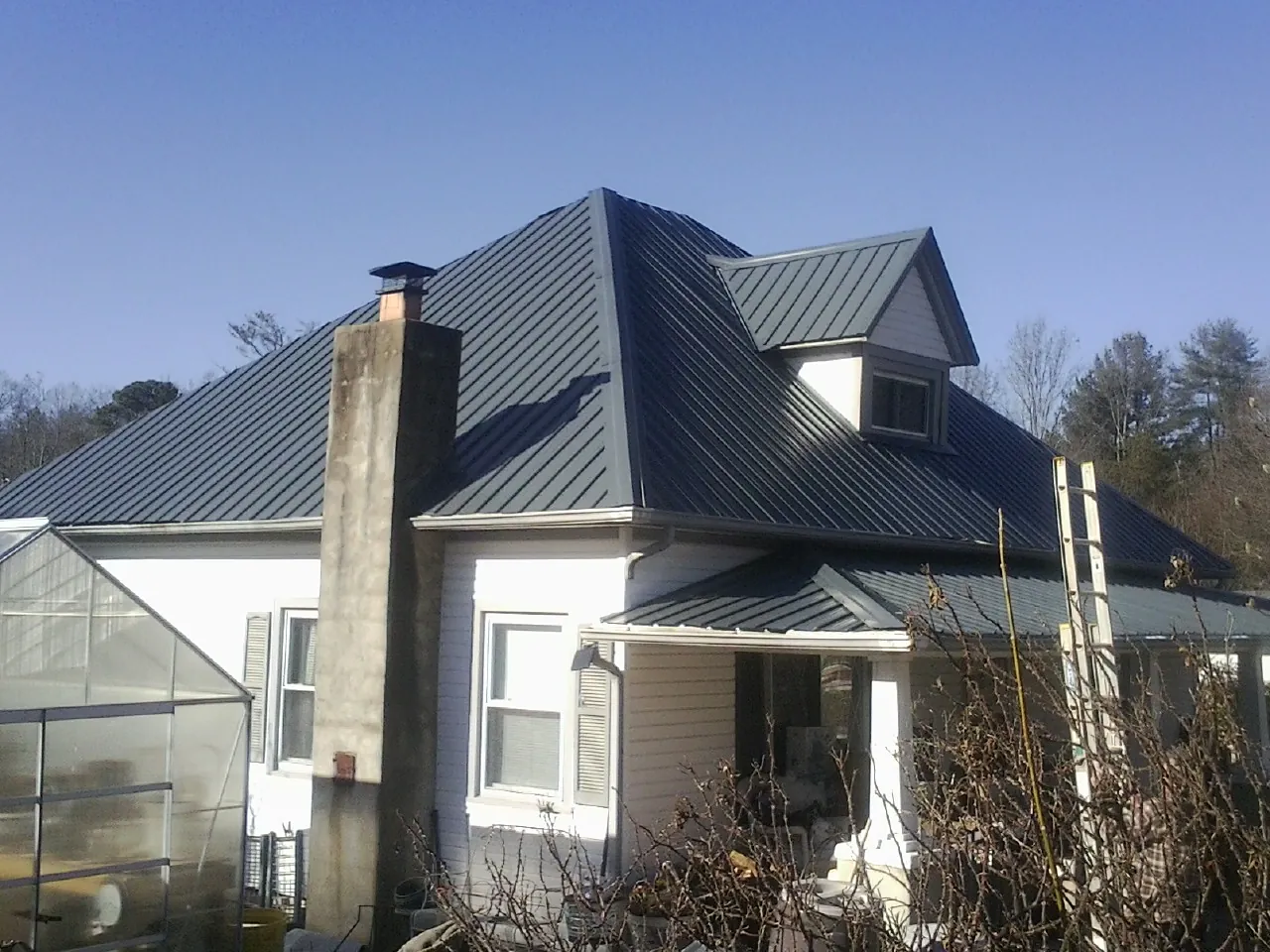 Dark blue standing seam metal roof on a white farmhouse with dormer — Slate & Tile Roof Repair by Roofing Brothers in Terrebonne