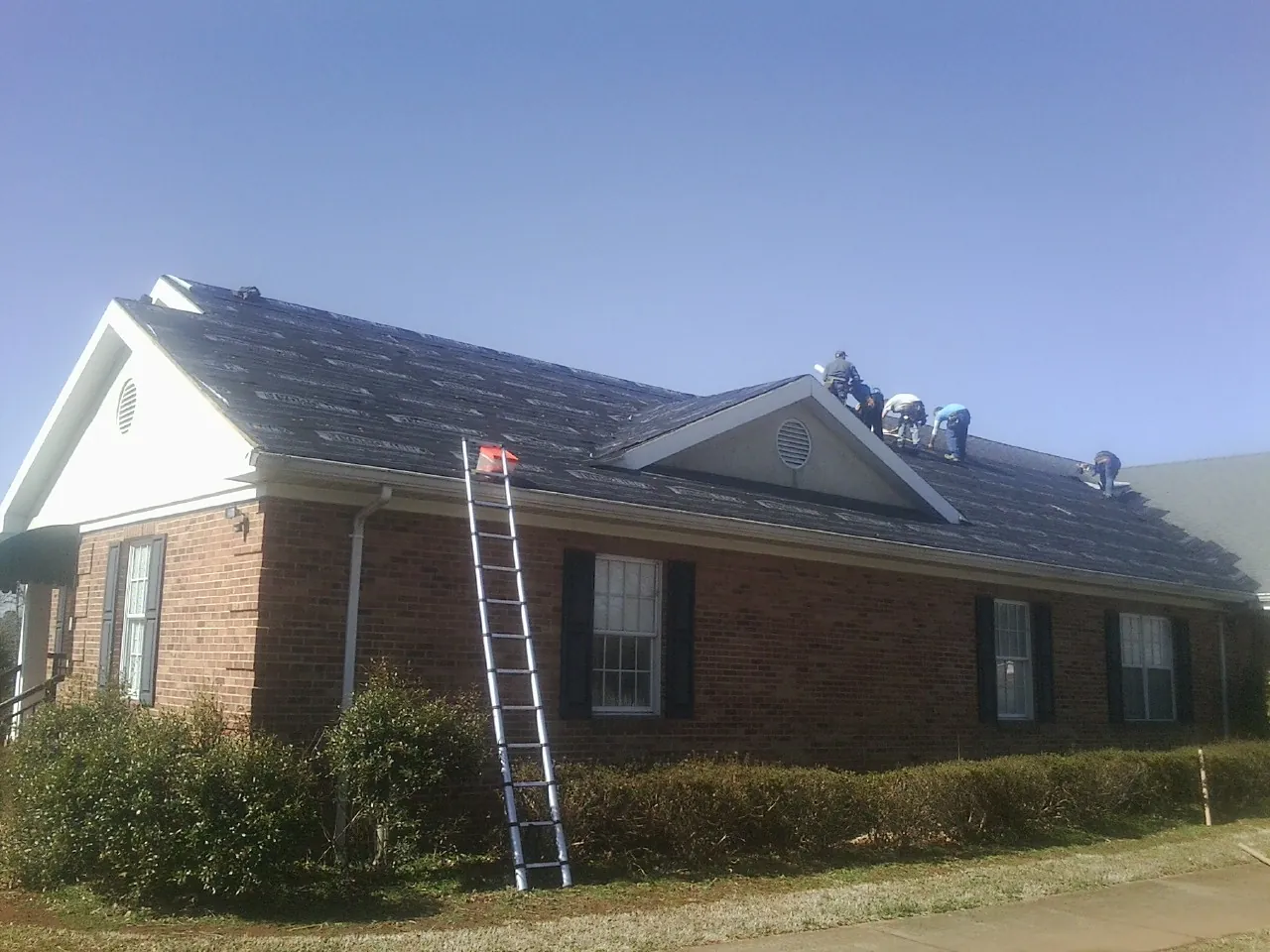 Crew tearing shingles off a brick ranch roof with a ladder set — Metal Roof Repair work by our crew in Terrebonne