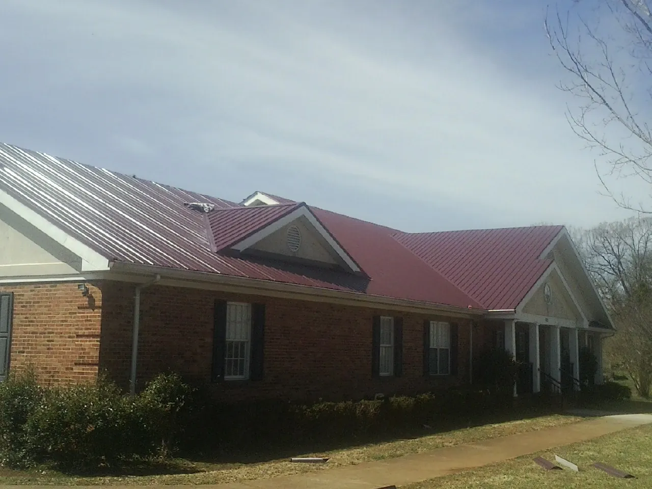 Red metal roof with gabled entries on a long brick building, from a Hail Damage Roof Repair job in Terrebonne