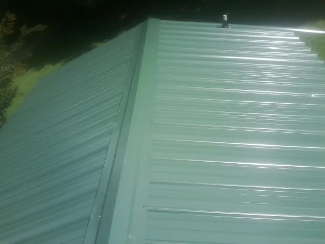 New green metal panels meeting at the ridge of a roof — Flat Roof Repair work by our crew in Terrebonne