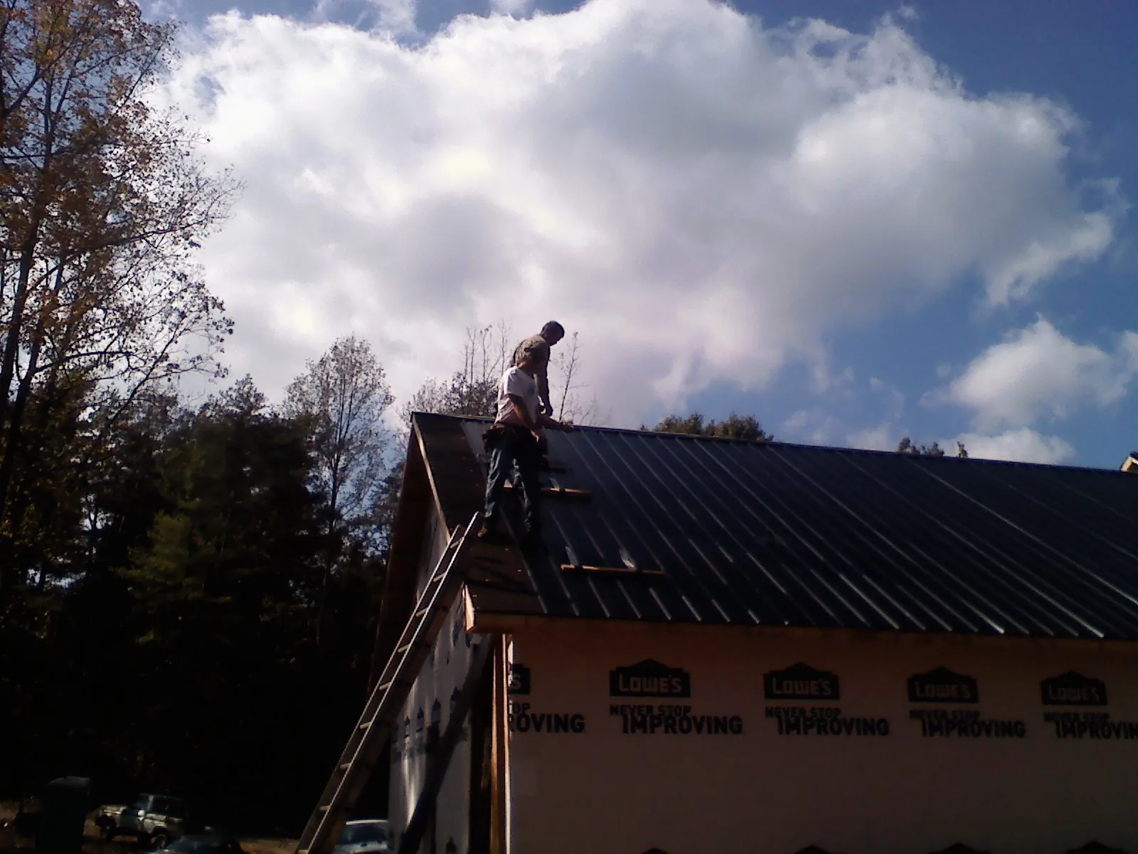 Roofer fastening dark metal panels high against a cloudy sky, from a Roof Inspection job in Terrebonne