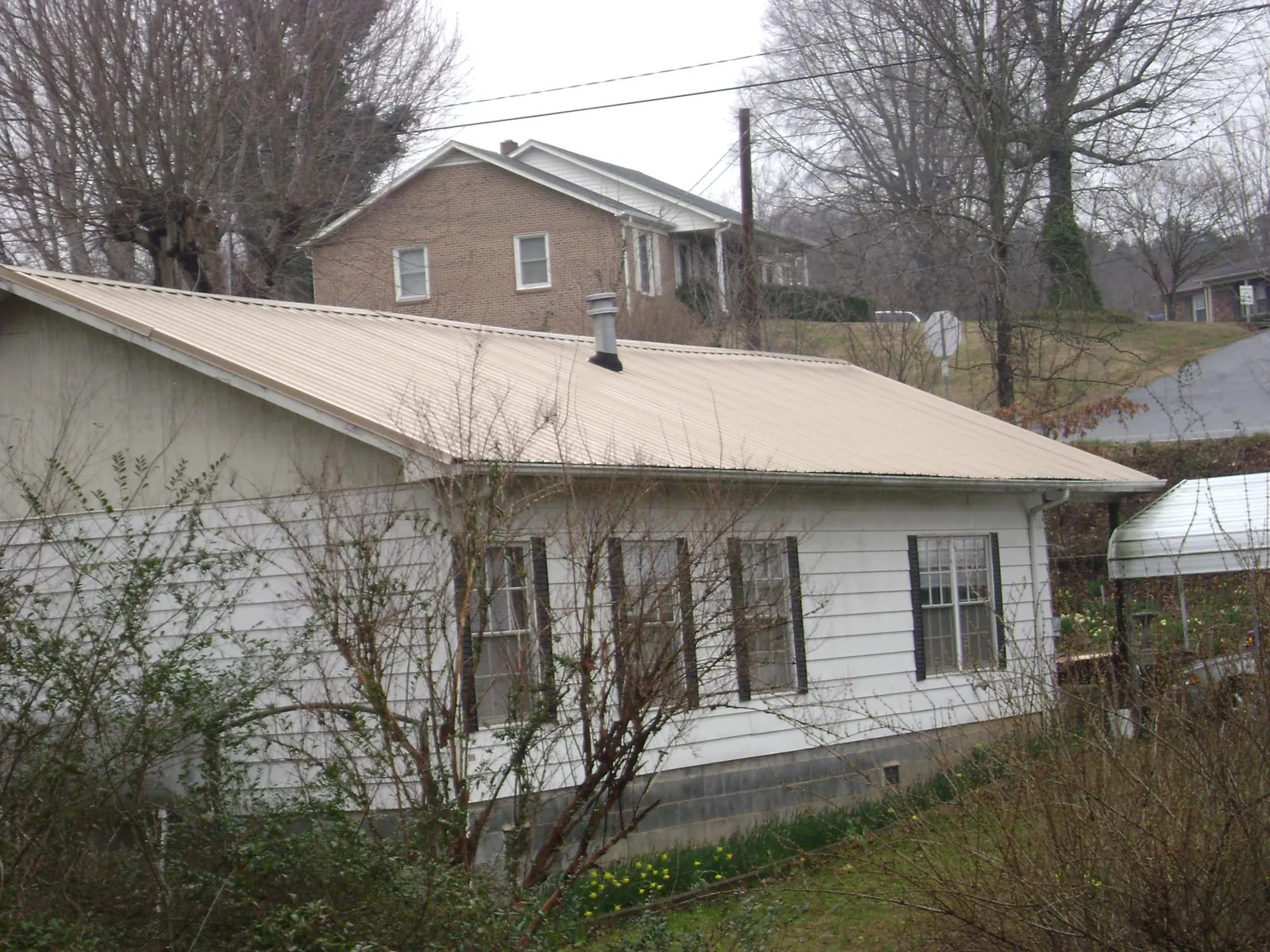Tan metal roof on a white sided house set into a hillside — Commercial Roofing by Roofing Brothers in Terrebonne