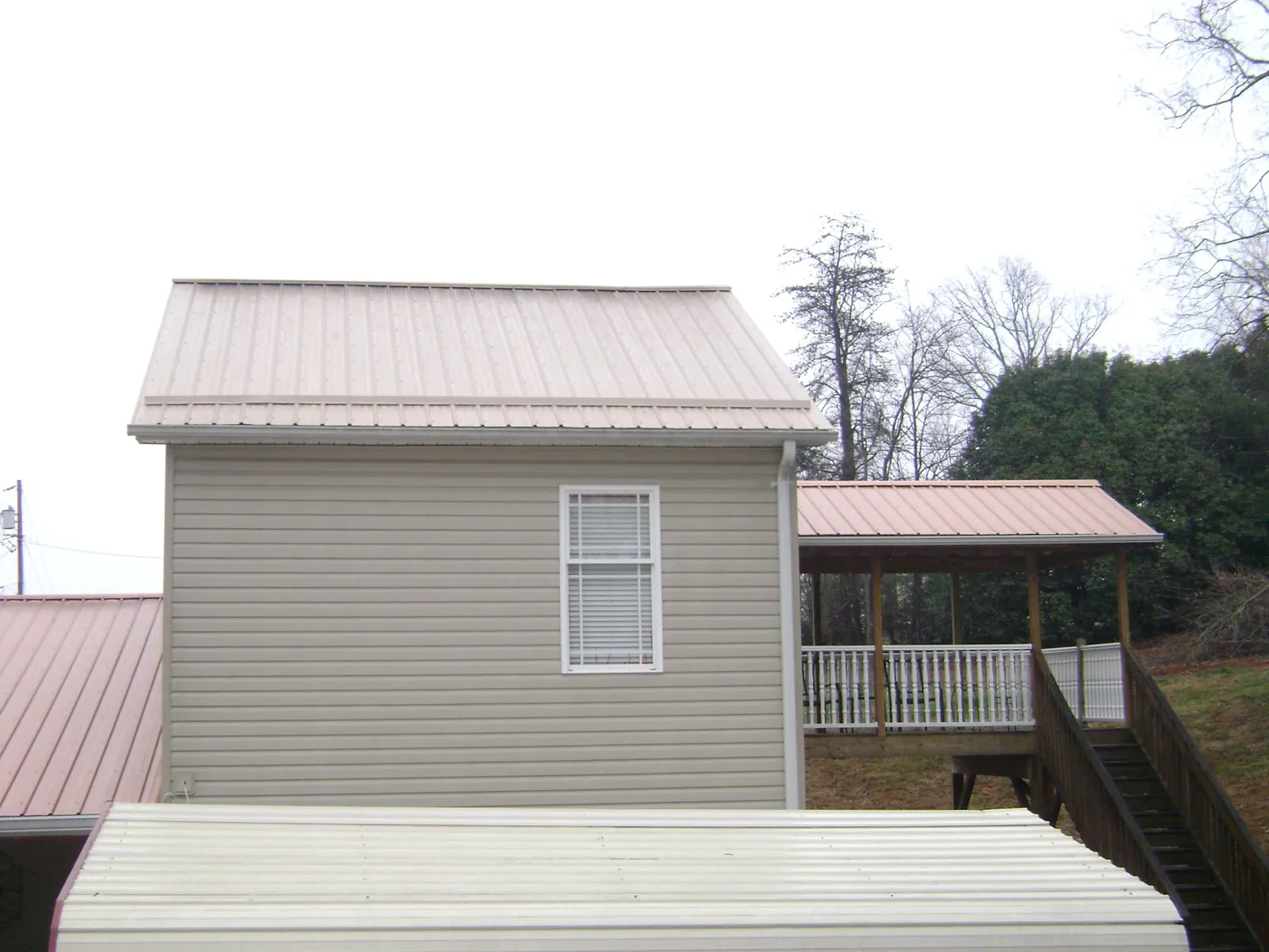 Tan metal roofs on a two story addition and attached porch, from a Roof Replacement job in Terrebonne